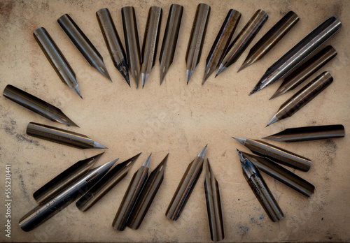 Numerous pen nibs displayed in a circular formation on a counter, some stained with ink; Studio photo