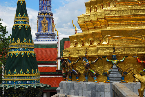Mosaic-covered spires and a gilded one held up by mythological beings.; Temple of the Emerald Buddha, The Grand Palace, Bangkok, Thailand. photo