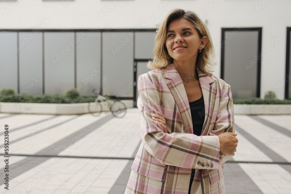Fototapeta premium Pretty young caucasian woman looking away with her arms crossed standing on street. Blonde wears casual shirt to work. Lifestyle concept