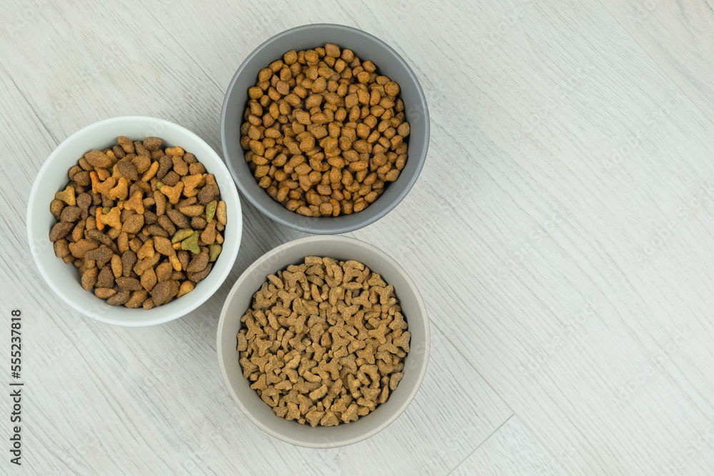 Variety of dry food for cats and dogs in ceramic bowls on a white wooden background. Copy space. Variety of dry food for cats and dogs in ceramic bowls on a white wooden background. Copy space.