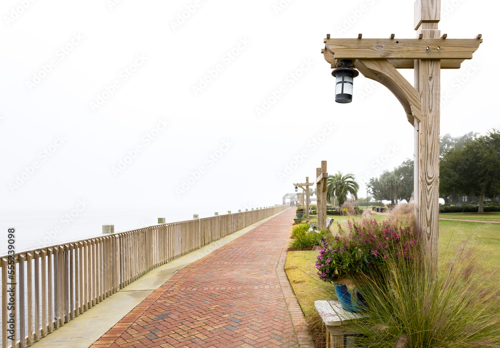 A brick sidewalk with a wood railing and pots with plants and unique light posts on a foggy day in the tropics.