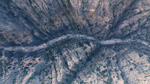 Aerial drone view of a deep canyon. High rocks. Narrow space. River below. Green trees grow along the rocks.