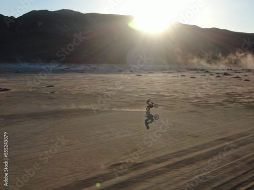 Dirt biker wheelie across dry lakebed in southern California desert at sunset photo