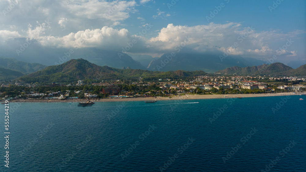 View from the sea to the coastal city. Sunny day. Green mountains. Aerial drone view. Landscape. Coastline. Boats.