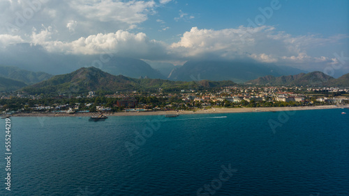 View from the sea to the coastal city. Sunny day. Green mountains. Aerial drone view. Landscape. Coastline. Boats.