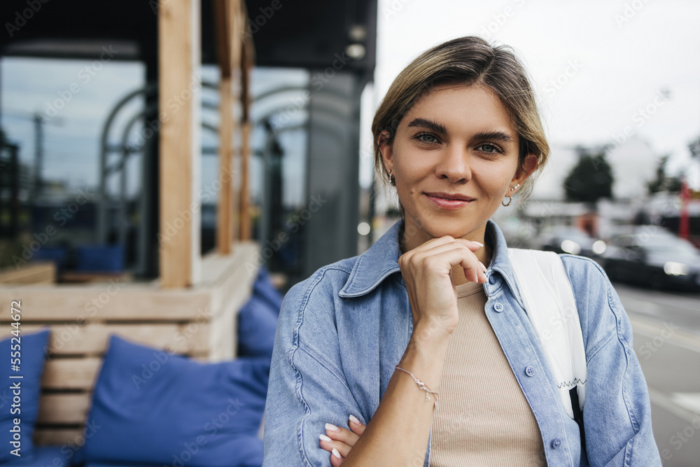 Cute young caucasian woman looking at camera standing outdoors during day. Blonde is wearing blue shirt. Good day concept Cute young caucasian woman looking at camera standing outdoors during day. Blonde is wearing blue shirt. Good day concept