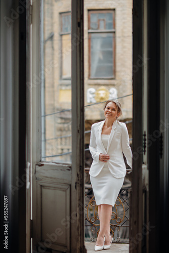 a beautiful, confident woman in a white suit on the balcony of the old building.