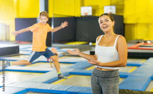 Teacher with children in trampoline center against background of children playing and jumping on a trampoline