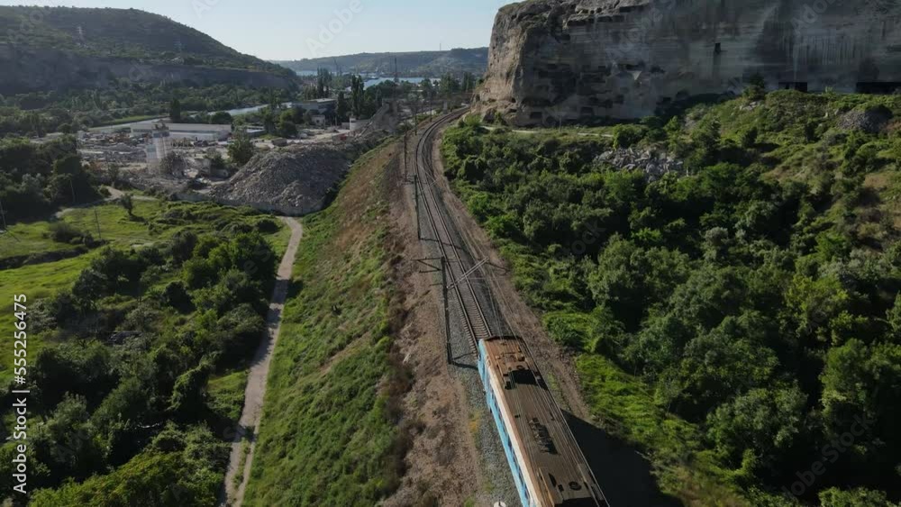 A cinematic flight overtaking an electric train traveling near a white cliff. The only railway