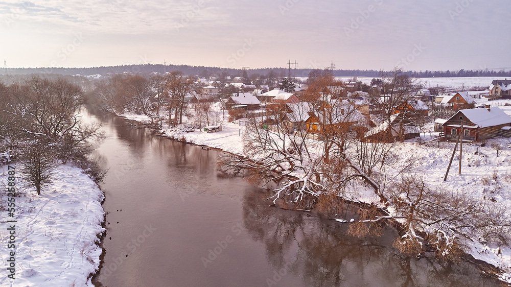 Winter river landscape, snow covered fields. Hoarfrost on trees, plants. Frosty evening. Sunny cloudy Misty weather. Cold season. Calm nature scene. Village