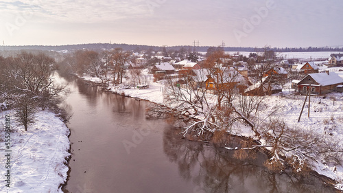 Obraz na płótnie Winter river landscape, snow covered fields. Hoarfrost on trees, plants. Frosty evening. Sunny cloudy Misty weather. Cold season. Calm nature scene. Village w salonie