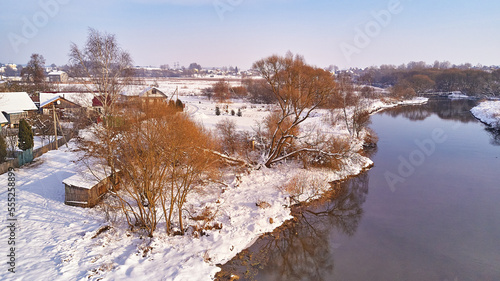 Obraz na płótnie Winter river landscape, snow covered fields. Hoarfrost on trees, plants. Frosty evening. Sunny cloudy Misty weather. Cold season. Calm nature scene. Village w salonie