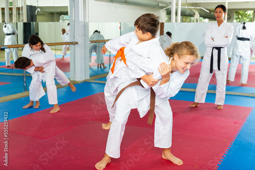 Teenager boy and girl, working in pair, mastering new karate moves in class with trainer