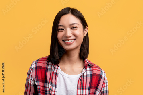 Happy person. Portrait of young asian lady with beautiful smile, looking at camera, posing in studio, yellow background