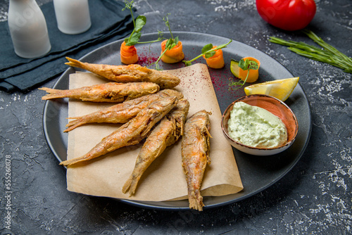 fried surmullet on black plate with sauce on dark table