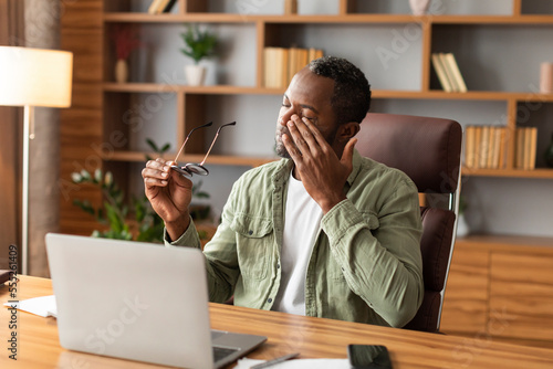 фотографія Tired sad mature black male takes off his glasses, rubbing eyes, suffering from