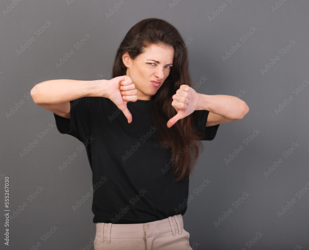 Beautiful fun angry casual unhappy woman in black t-shirt showing deslike sign by two hands demonstrated negative signal on empty copy space background. Beautiful fun angry casual unhappy woman in black t-shirt showing deslike sign by two hands demonstrated negative signal on empty copy space background.