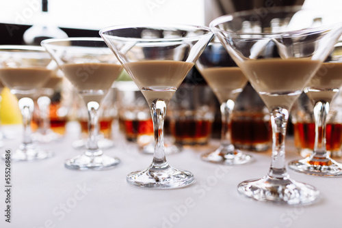 Many martini glasses with alcohol cream coffee irish cocktail, on white table background. Irish cream baileys liqueur for party. Trendy autumn winter alcohol drink.