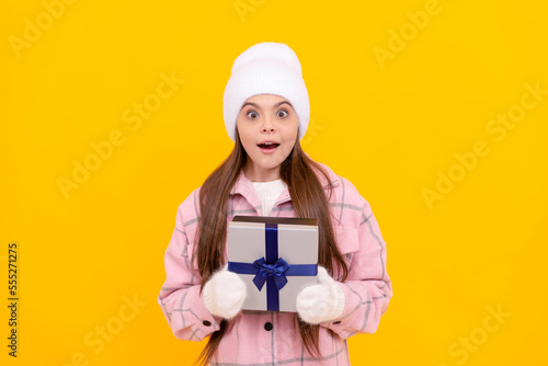 shocked kid in hat and mittens hold gift box on yellow background, xmas