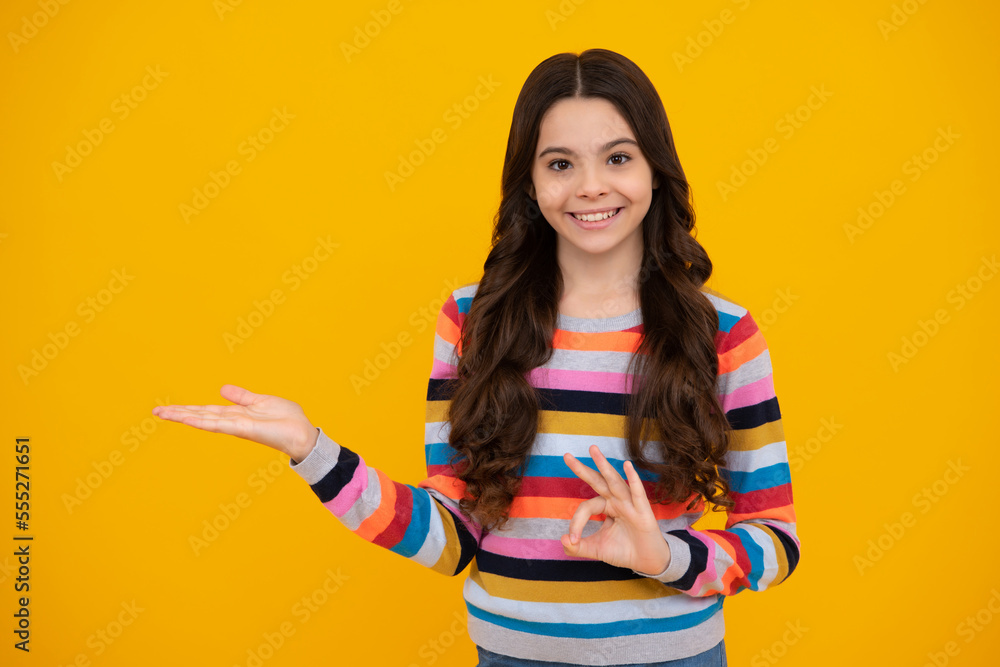 Happy teenager, positive and smiling emotions of teen girl. Portrait of cute teenager child girl pointing hand showing adverts with copy space over yellow background. Happy teenager, positive and smiling emotions of teen girl. Portrait of cute teenager child girl pointing hand showing adverts with copy space over yellow background.