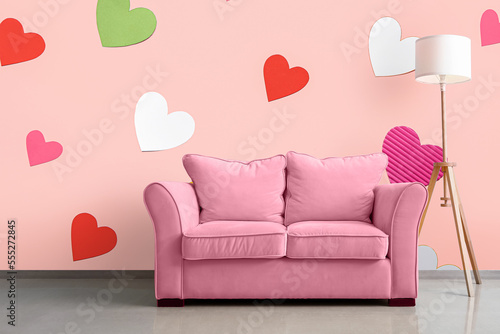 Pink sofa with lamp near pink wall with printed colorful hearts in room