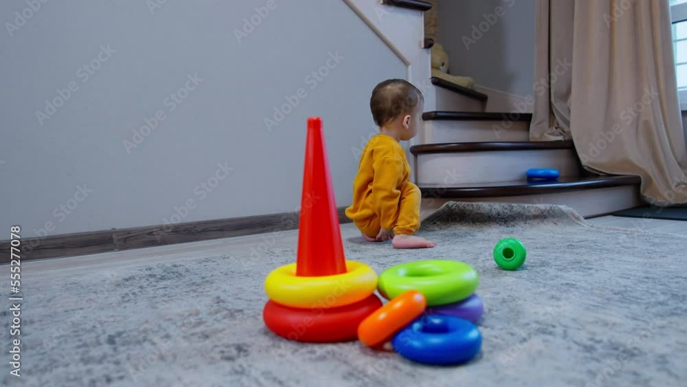 Sweet baby boy in orange sport suit plays with toy pyramid in the room. Little child takes the parts of toy and puts them on the stairs. Sweet baby boy in orange sport suit plays with toy pyramid in the room. Little child takes the parts of toy and puts them on the stairs.