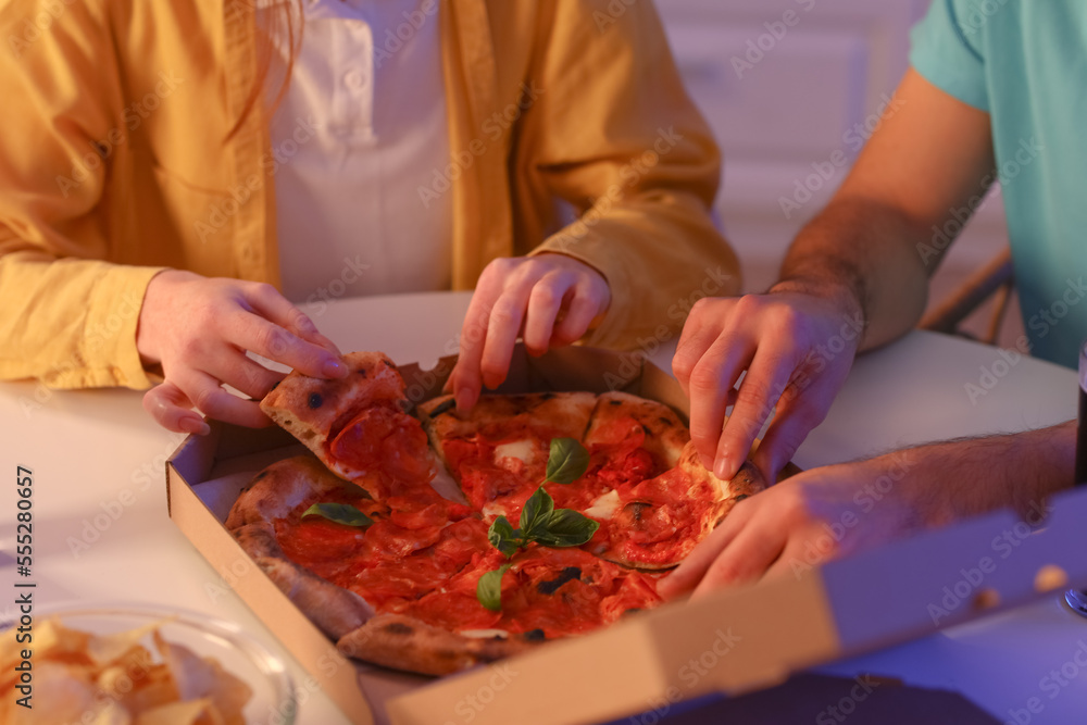 Young couple eating tasty pizza in kitchen at night, closeup