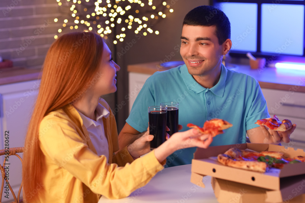 Young couple eating tasty pizza and drinking cola in kitchen at night Young couple eating tasty pizza and drinking cola in kitchen at night