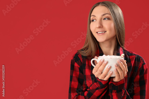 Young woman in pajamas with cup of cocoa on red background  closeup