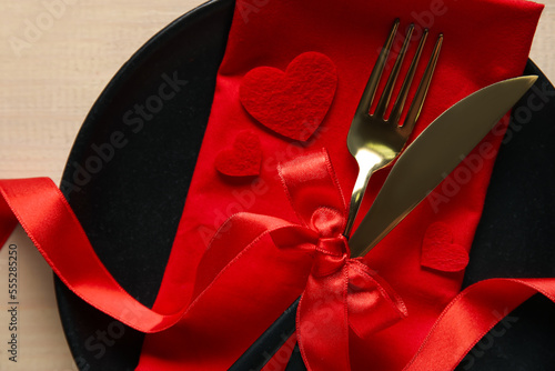 Table setting for Valentine's Day with red hearts and bow on wooden background, closeup