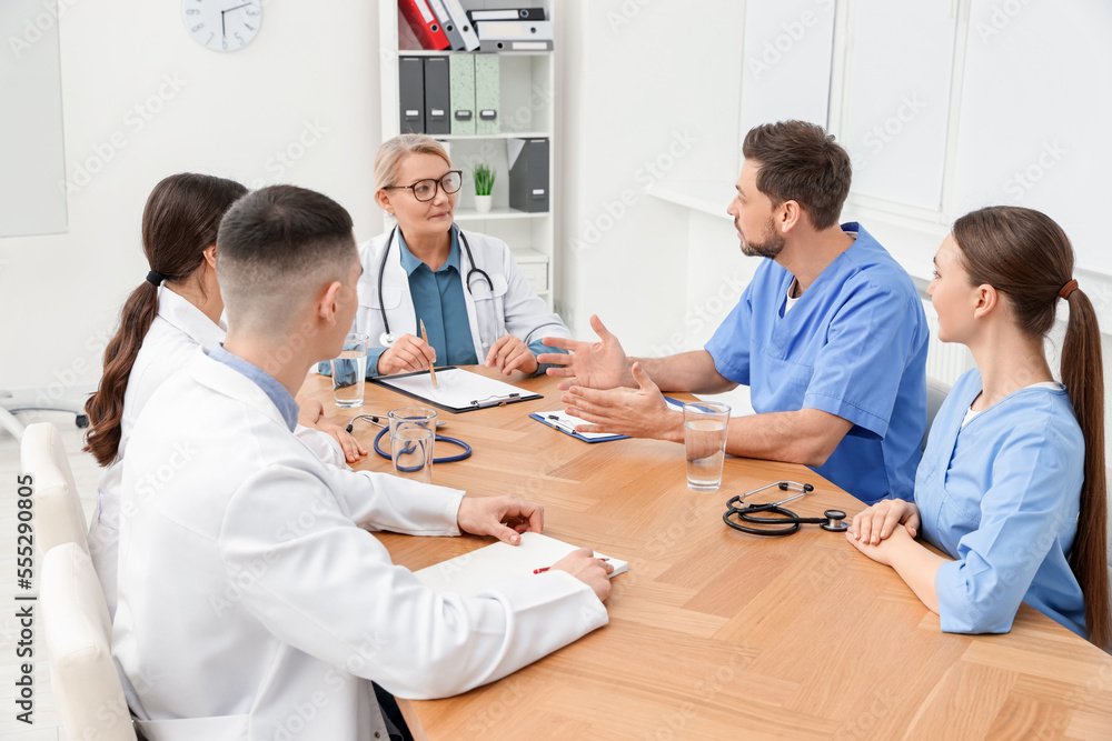 Medical conference. Team of doctors having discussion with speaker at wooden table in clinic Medical conference. Team of doctors having discussion with speaker at wooden table in clinic
