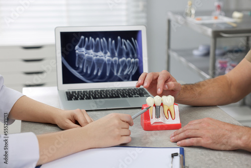 Doctor showing patient educational model of dental implant in clinic, closeup photo