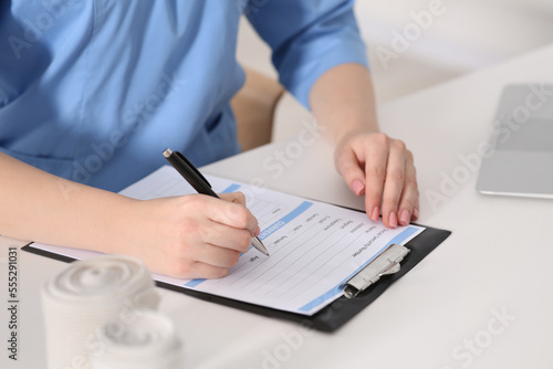 Doctor filling patient's medical card at table in clinic, closeup