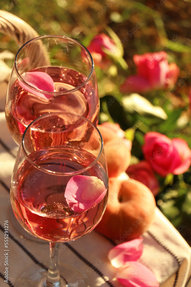 Glasses of delicious rose wine with petals on white picnic blanket outside Glasses of delicious rose wine with petals on white picnic blanket outside