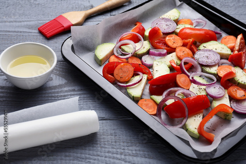 Baking pan with parchment paper and raw vegetables on grey wooden table
