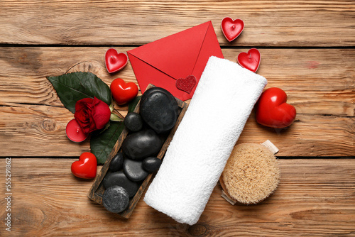 Beautiful spa composition for Valentine's Day with envelope, stones, candles, towel, hearts and rose on wooden background