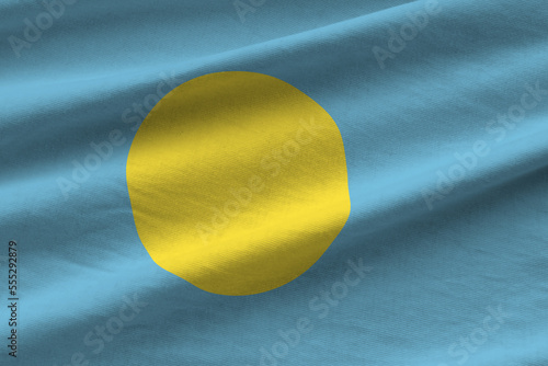 Palau flag with big folds waving close up under the studio light indoors. The official symbols and colors in fabric banner photo