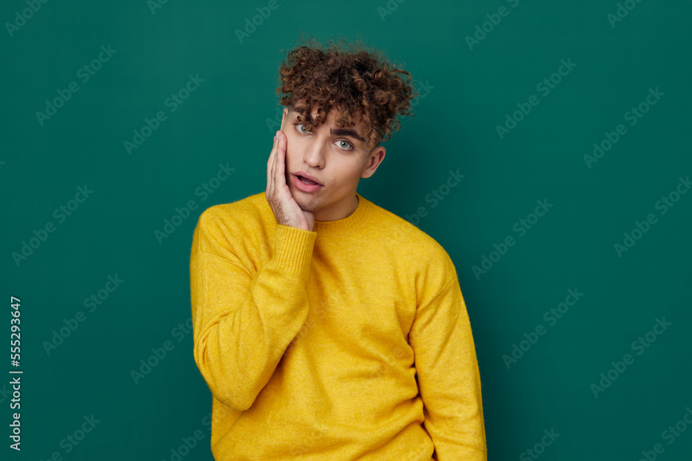 a shocked man in a yellow sweater stands on a green background and holds his head with his hand, his mouth wide open, looking into the camera from shock a shocked man in a yellow sweater stands on a green background and holds his head with his hand, his mouth wide open, looking into the camera from shock