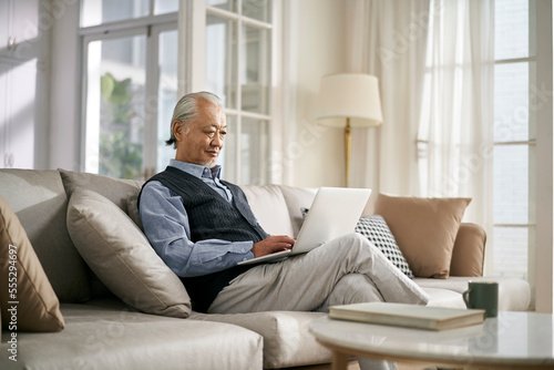 senior asian man sitting on couch looking at notebook computer