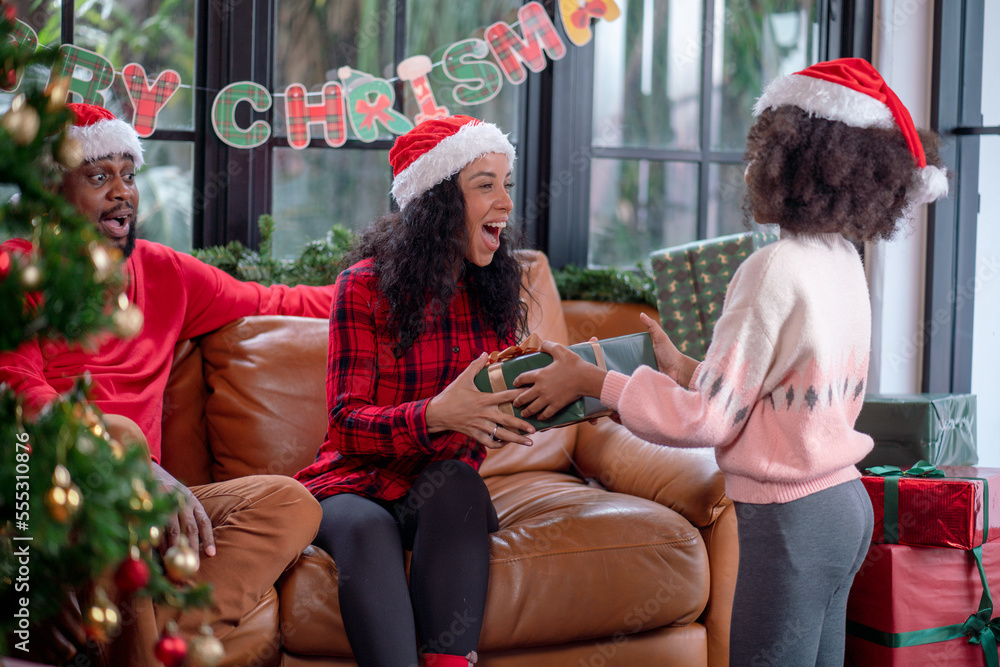 Christmas family. Daughter is holding a gift box for her parents. At home near the Christmas tree. Christmas family. Daughter is holding a gift box for her parents. At home near the Christmas tree.