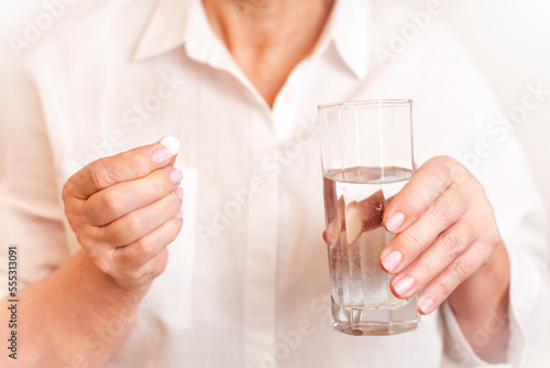 woman holding a pill and a glass of water in her hands close-up