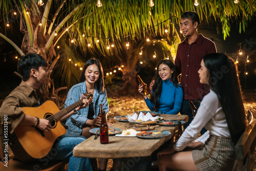 Portrait of Happy Asian group of friends having fun to music dining and drinking together outdoor - Happy friends group toasting beers - People, food, drink lifestyle, new year celebration concept.
