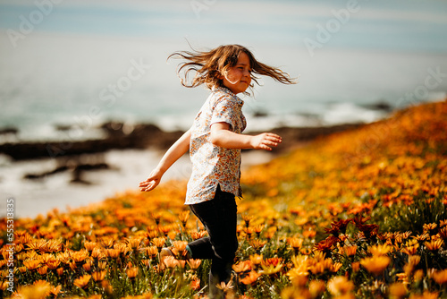 Boy spinning in field of flowers on clifftop next to the ocean photo