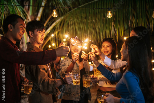 Portrait of Happy Asian group of friends having fun with sparklers outdoor - Young people having fun with fireworks at night time - People, food, drink lifestyle, new year celebration concept.
