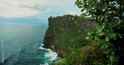 Pristine tropical green beach with Uluwatu Temple Pura Luhur Hindu on huge cliff abyss and endless ocean horizon on Bali island. Summer holiday vacation. Balinese sea water and rocky coastline. photo