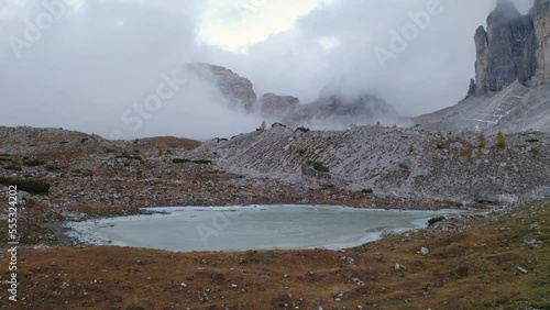 4k drone forward video (Ultra High Definition) of Cime Di Lavaredo National Park in the morning mist. Gloomy autumn view of frozen Rienzquelle lake. Trekking in Dolomite Alps, Italy, Europe. photo