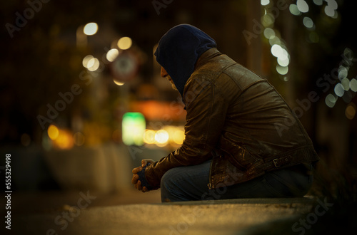 Side view of adult man sitting on stone bench on street at night