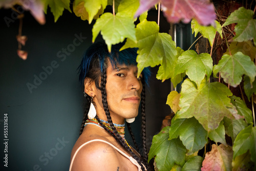 Behang indigenous non-binary artist in garden doorway with vine