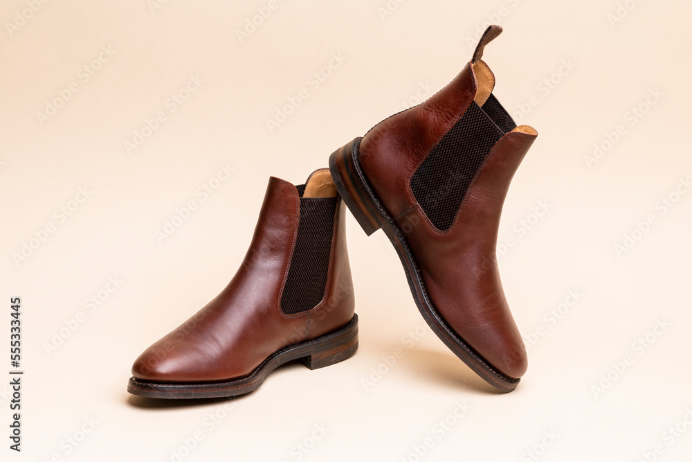Footwear ideas. Pair of Classic Leather Chealsea Boots As Still Life Concepts Placed Over Beige Background. Footwear ideas. Pair of Classic Leather Chealsea Boots As Still Life Concepts Placed Over Beige Background.