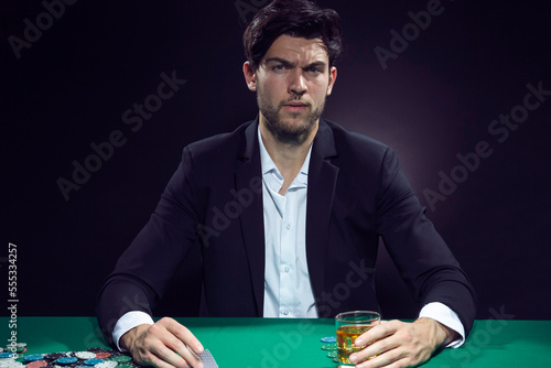 Gambling Ideas. One Concentrated Thoughful Handsome Caucasian Brunet Cards Player At Pocker Table With Chips and Cards While Playing and Drinking